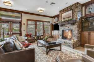 Interior community clubhouse, Lounge area with leather seats arranged around the stone fireplace, Tile floor, large neutral area rug, television in clubhouse, dark brown cabinetry.