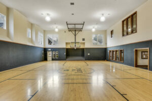 Community Indoor Basketball Court, Full-Size, Ceiling mounted Basketball hoops, Small Bleacher area.