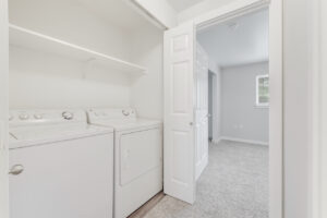 Linen Closet, Washer and dryer, white walls, wood like floors in linen closet, neutral toned carpeting in hallway.