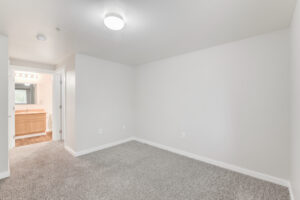 Interior Unit Bedroom, ceiling light fixture, white walls, neutral toned carpeting, wood-like floors in bathroom.