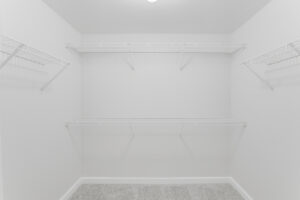 Interior Unit Master bedroom walk-in closet, 4 shelves with hanging racks, white walls, neutral toned carpeting.