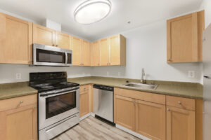 Interior Unit Kitchen, wood-like floors, light brown cabinets, stainless steel appliances, ceiling light fixture, laminate countertops.