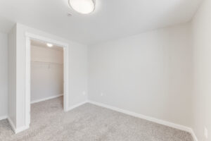 Interior Unit Bedroom, ceiling light fixture, walk-in closet, white walls, neutral toned carpeting.